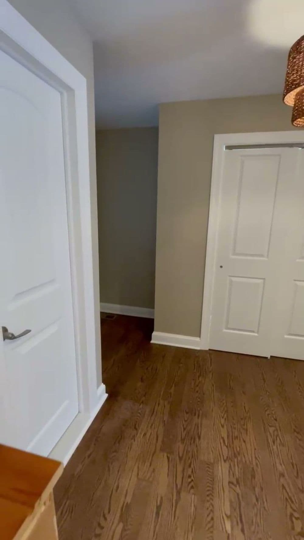 Interior hallway featuring white doors, light gray walls, and hardwood flooring.